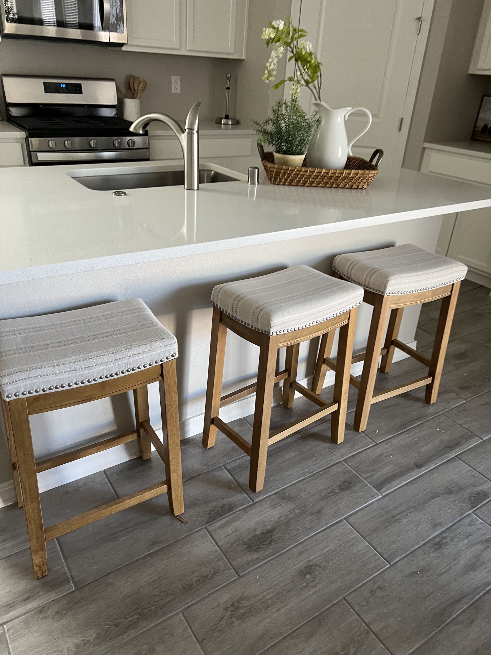 Three wooden stools are sitting on a tiled floor in a kitchen.