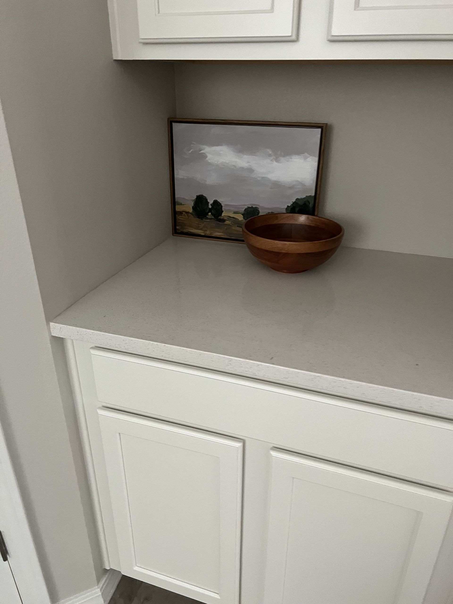 A wooden bowl is sitting on a counter next to a painting.