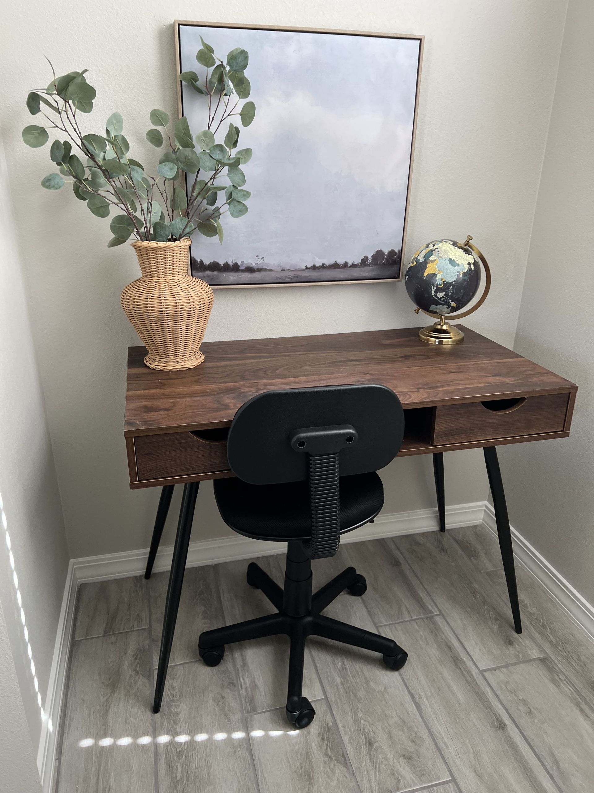 A wooden desk with a black chair and a globe on it.