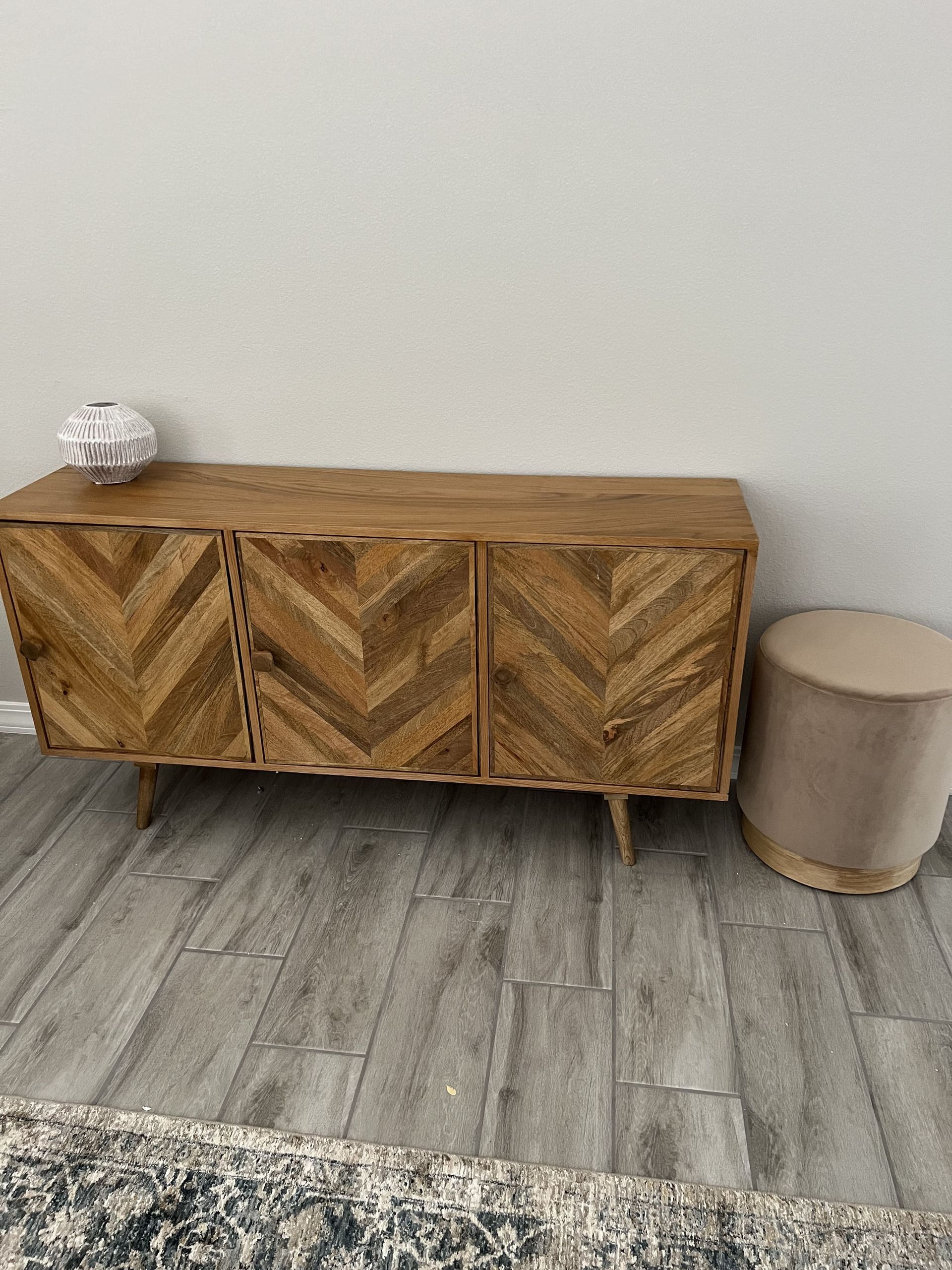 A wooden dresser is sitting on a wooden floor next to an ottoman.