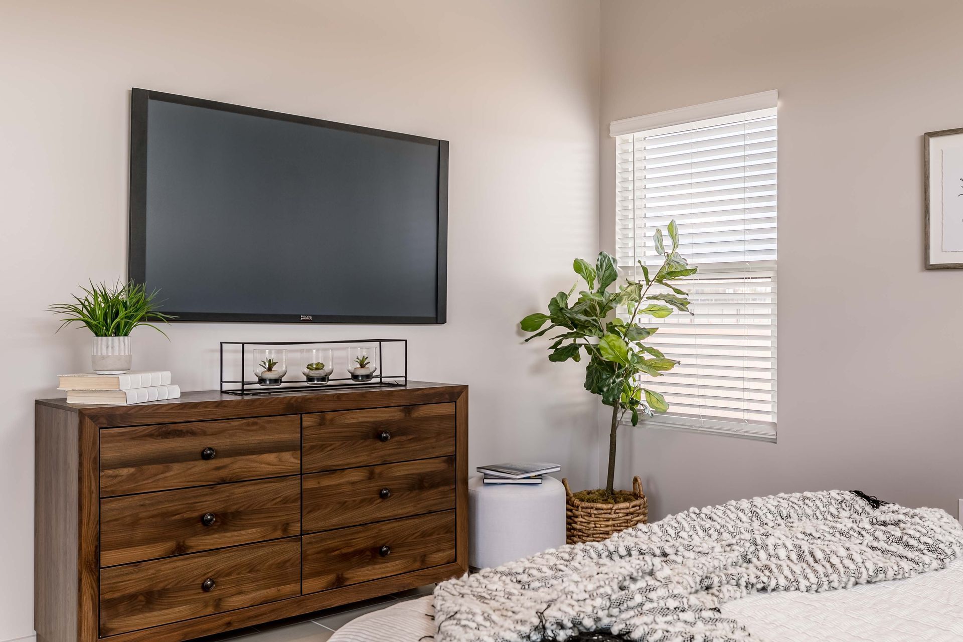 A bedroom with a large flat screen tv on the wall above a wooden dresser.