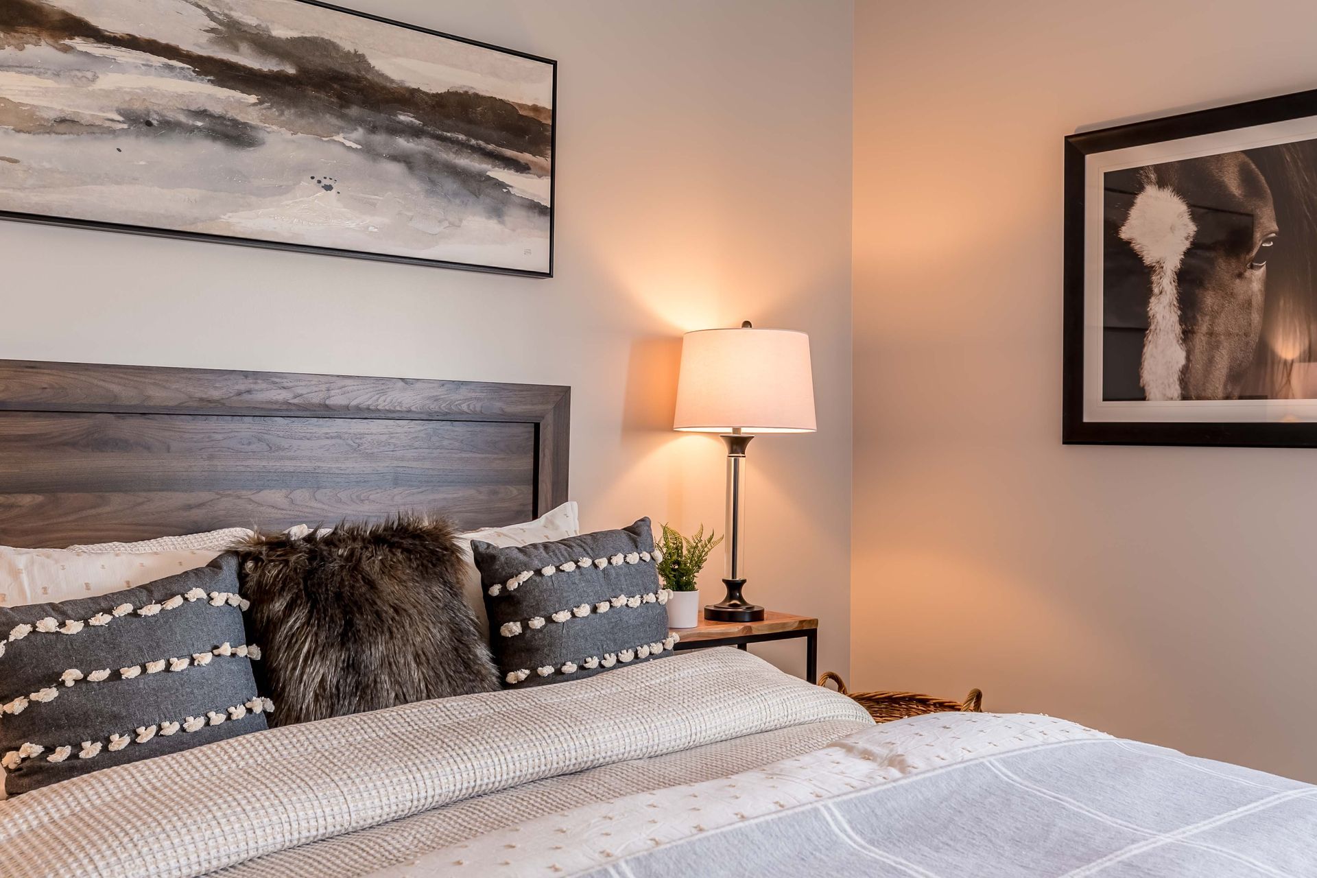 A bedroom with a bed , lamp , nightstand and painting on the wall.