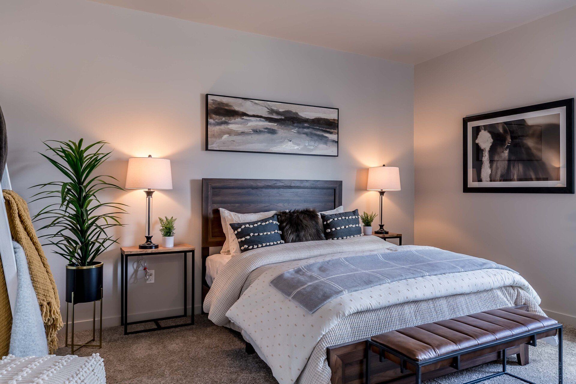 A bedroom with a bed , lamps , a bench and a picture on the wall.