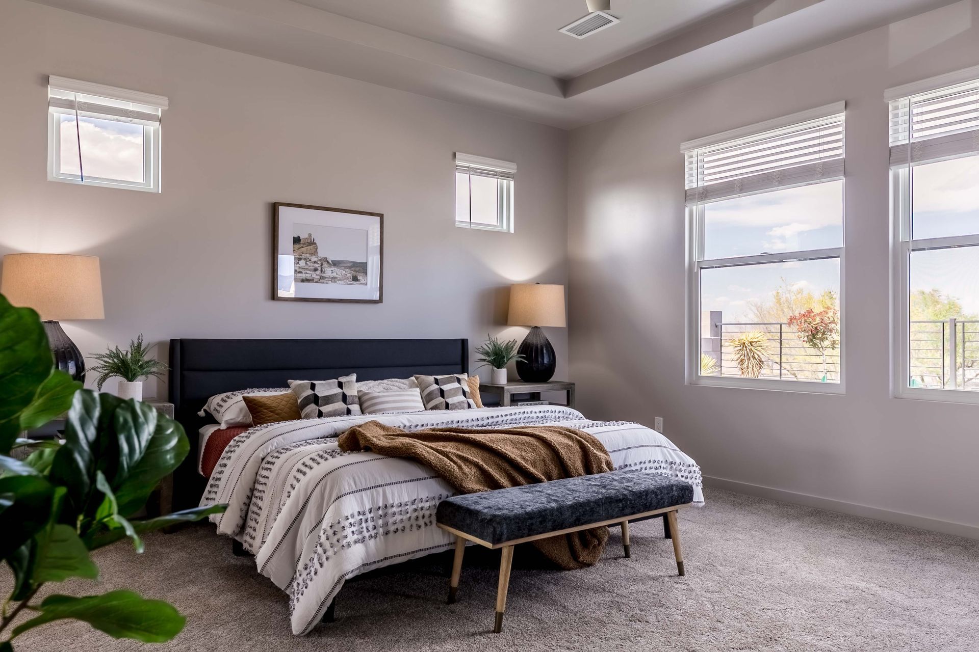A bedroom with a bed , bench , lamps and windows.