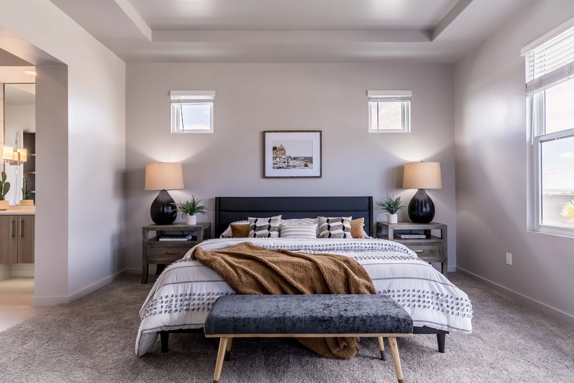 A bedroom with a bed , nightstands , lamps and a bench.