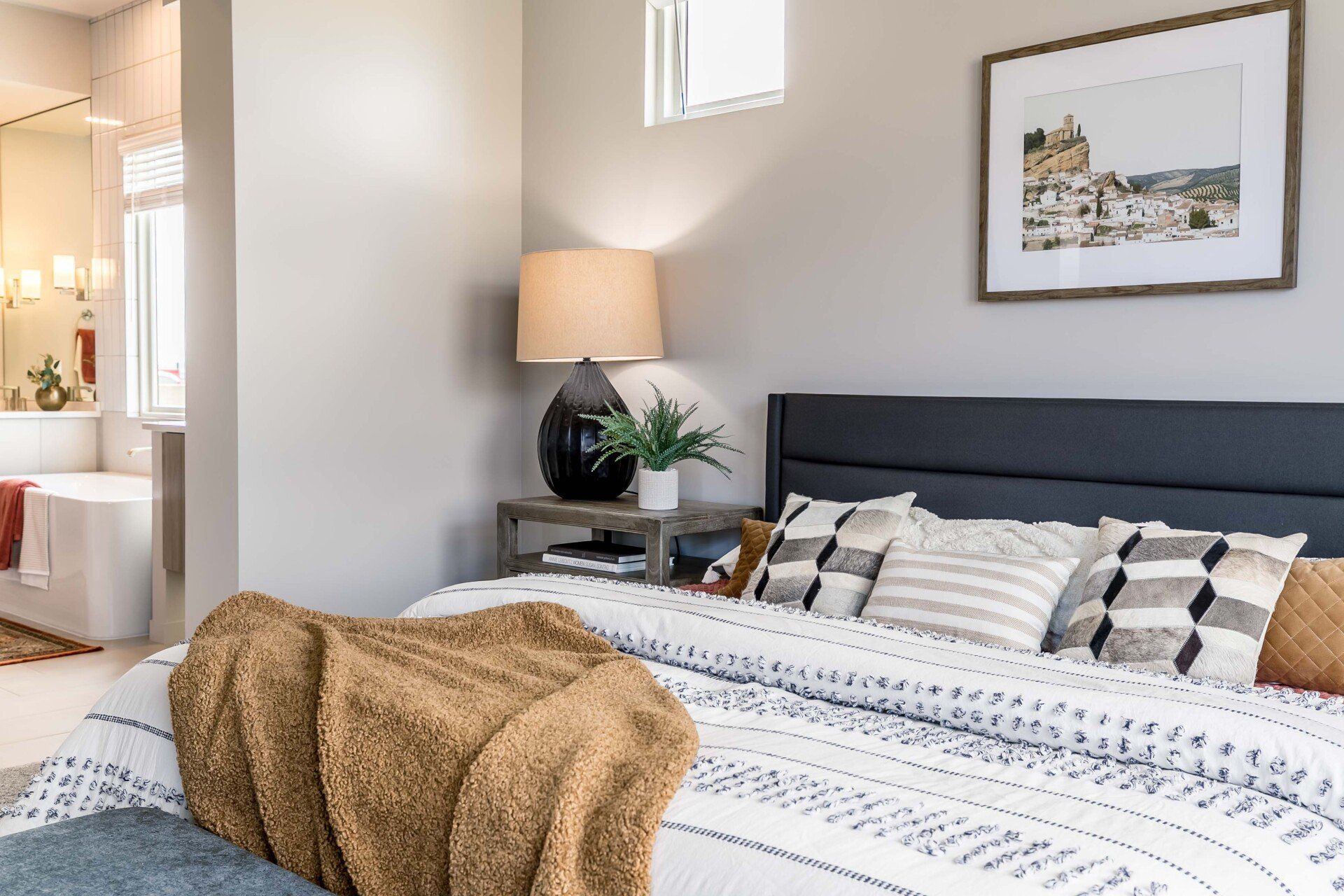 A bedroom with a bed , nightstand , lamp and picture on the wall.