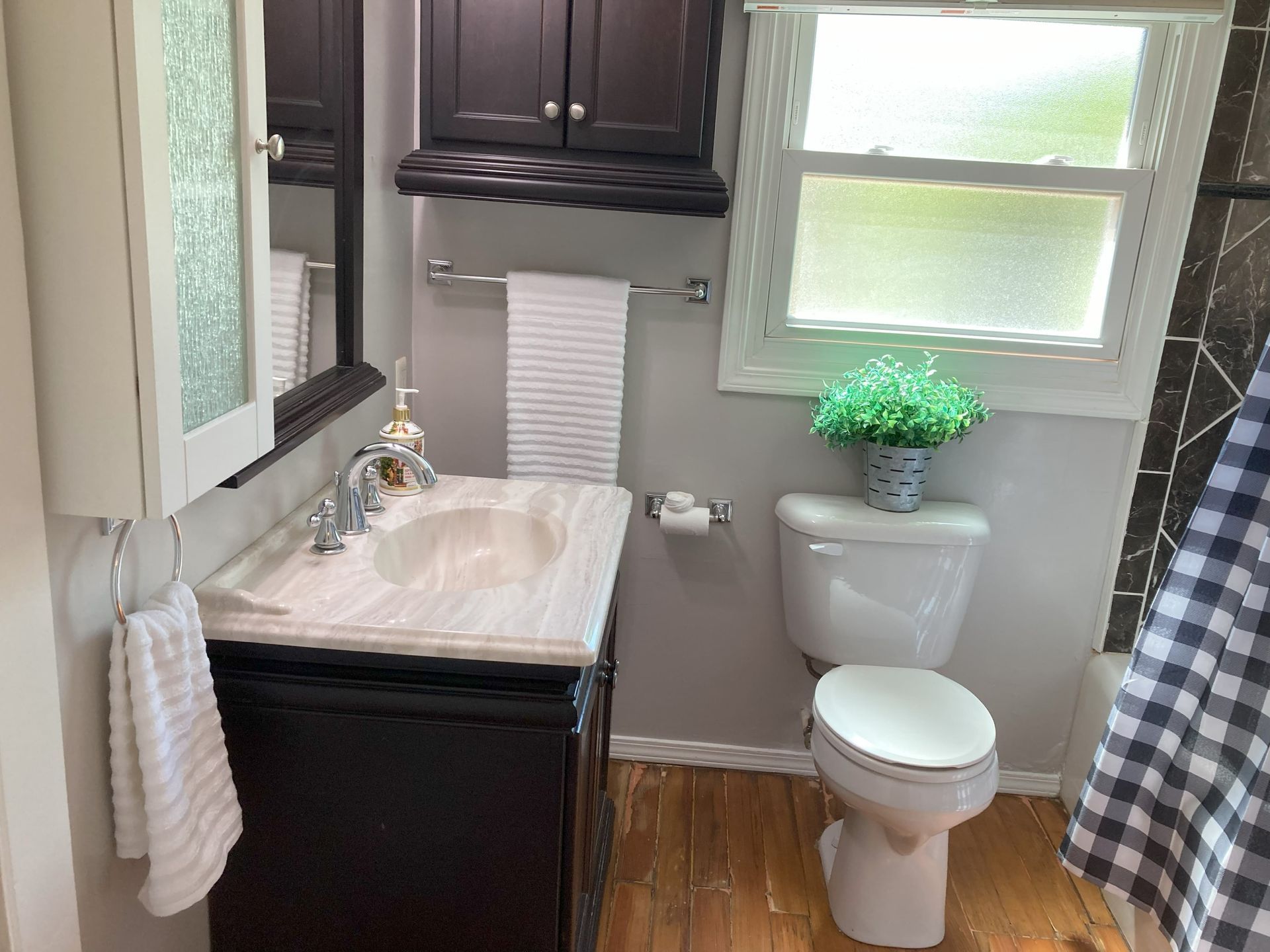 A bathroom with a sink , toilet , mirror and window.