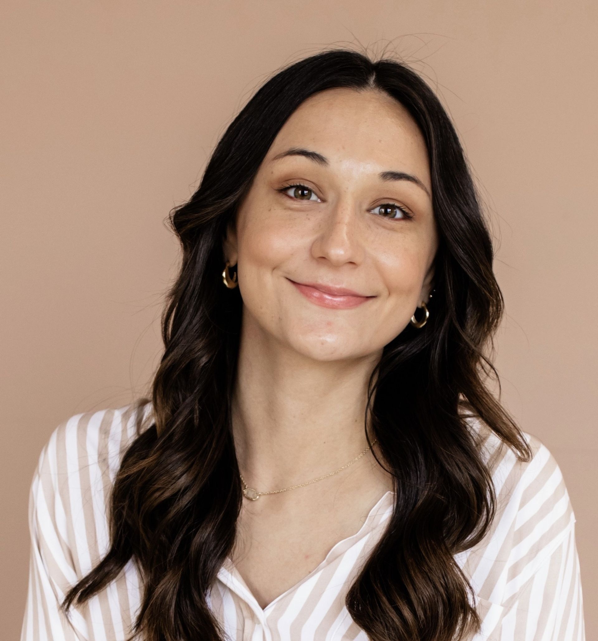 A woman wearing a striped shirt and earrings is smiling for the camera.