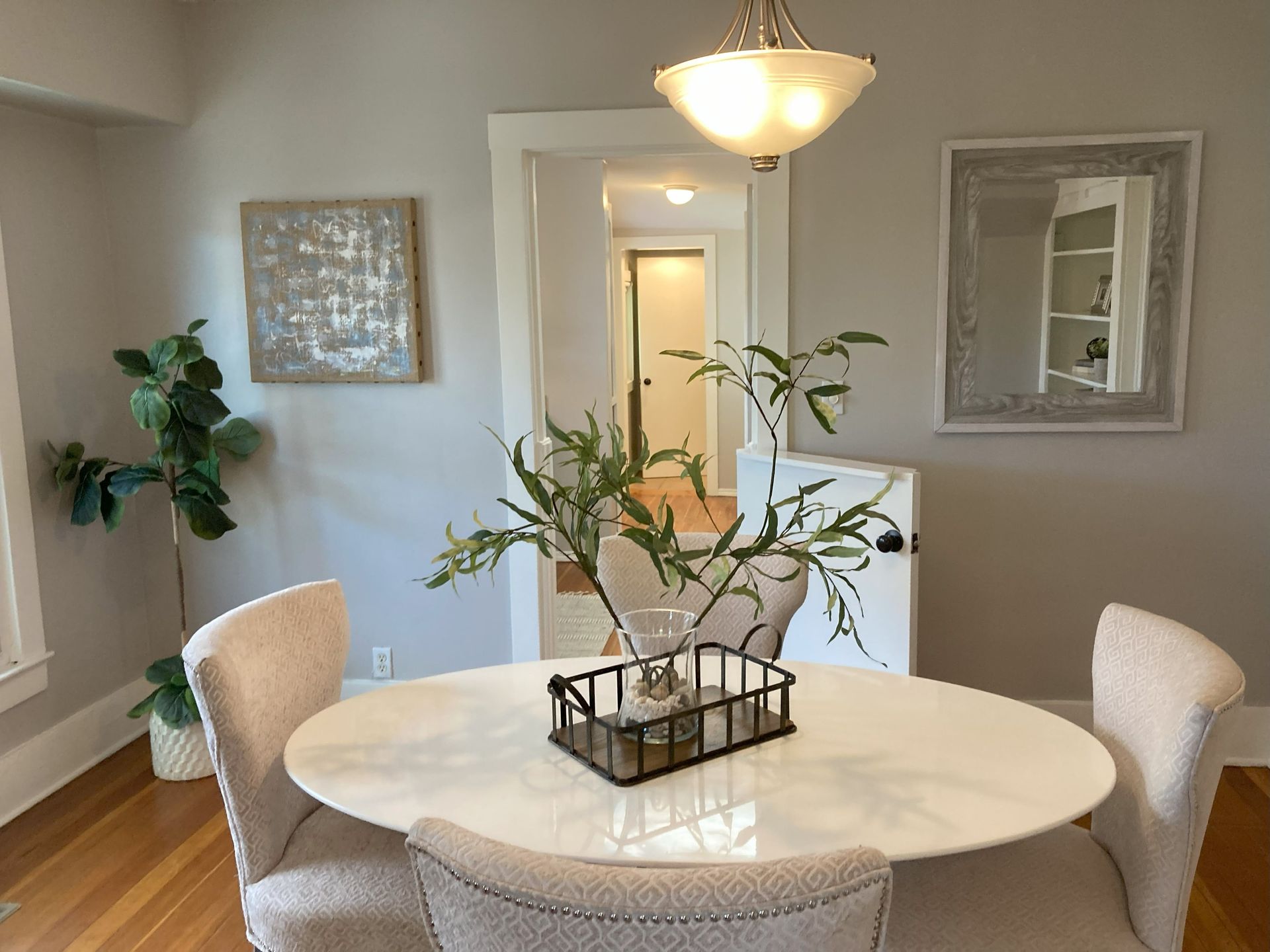 A dining room with a white table and chairs and a plant on it.