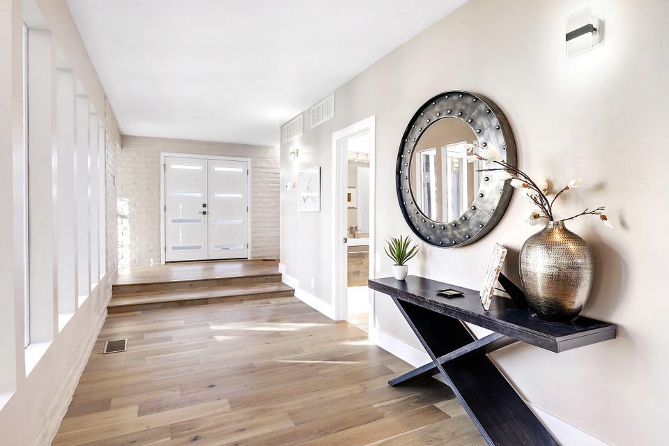 A hallway with a table , mirror and vase.