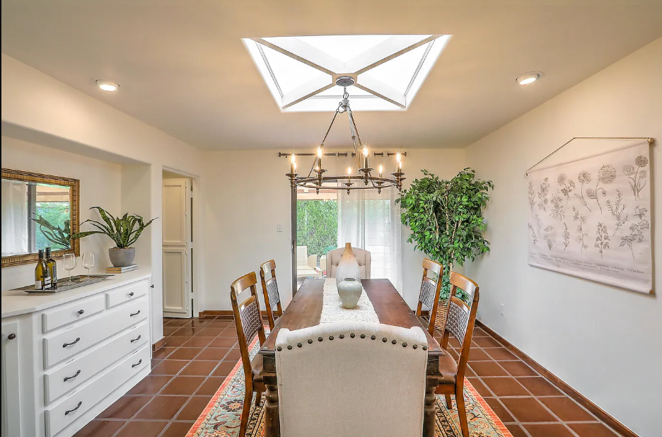 A dining room with a long table and chairs and a skylight.