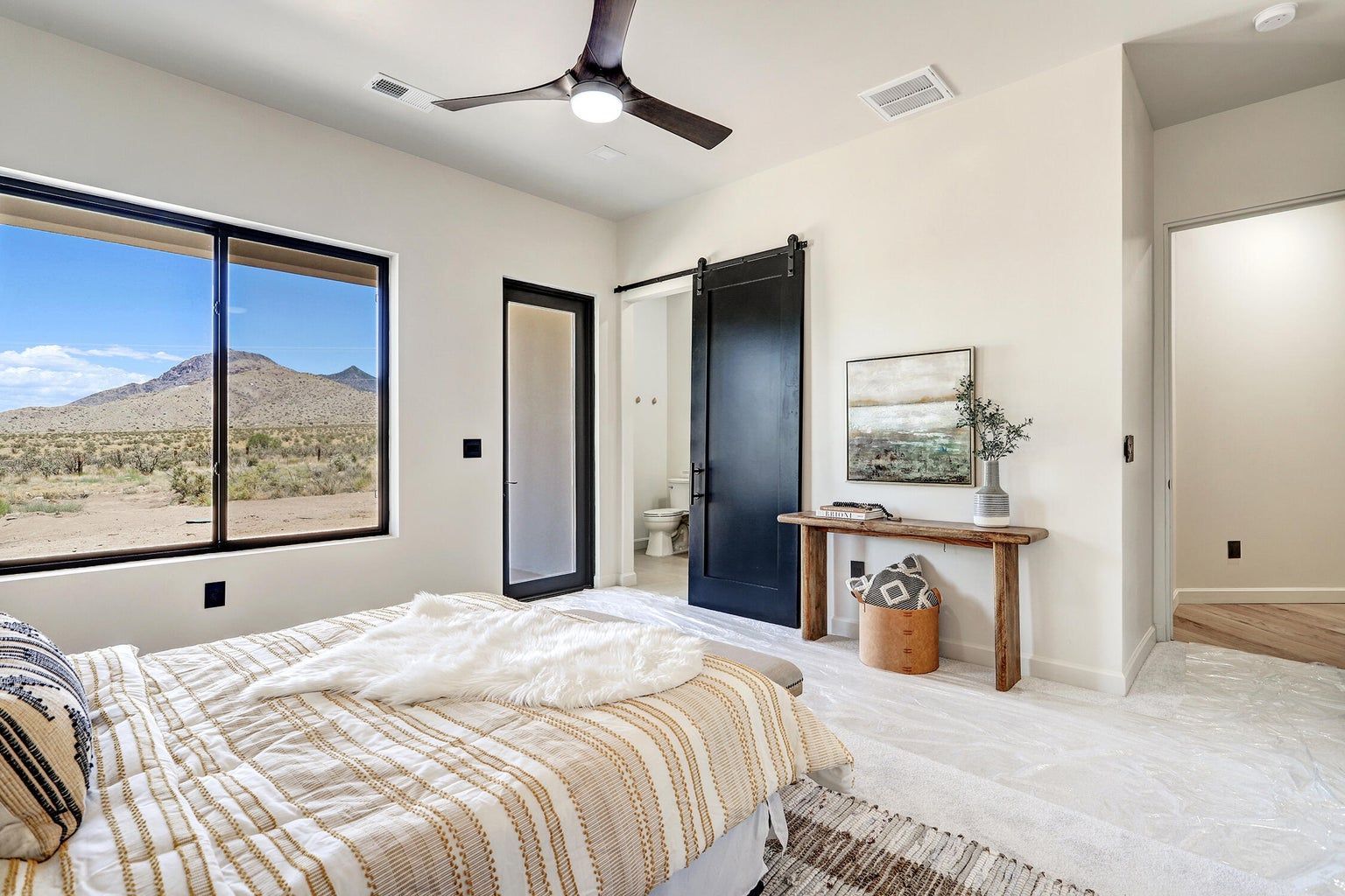 A bedroom with a bed , ceiling fan , window and sliding barn door.