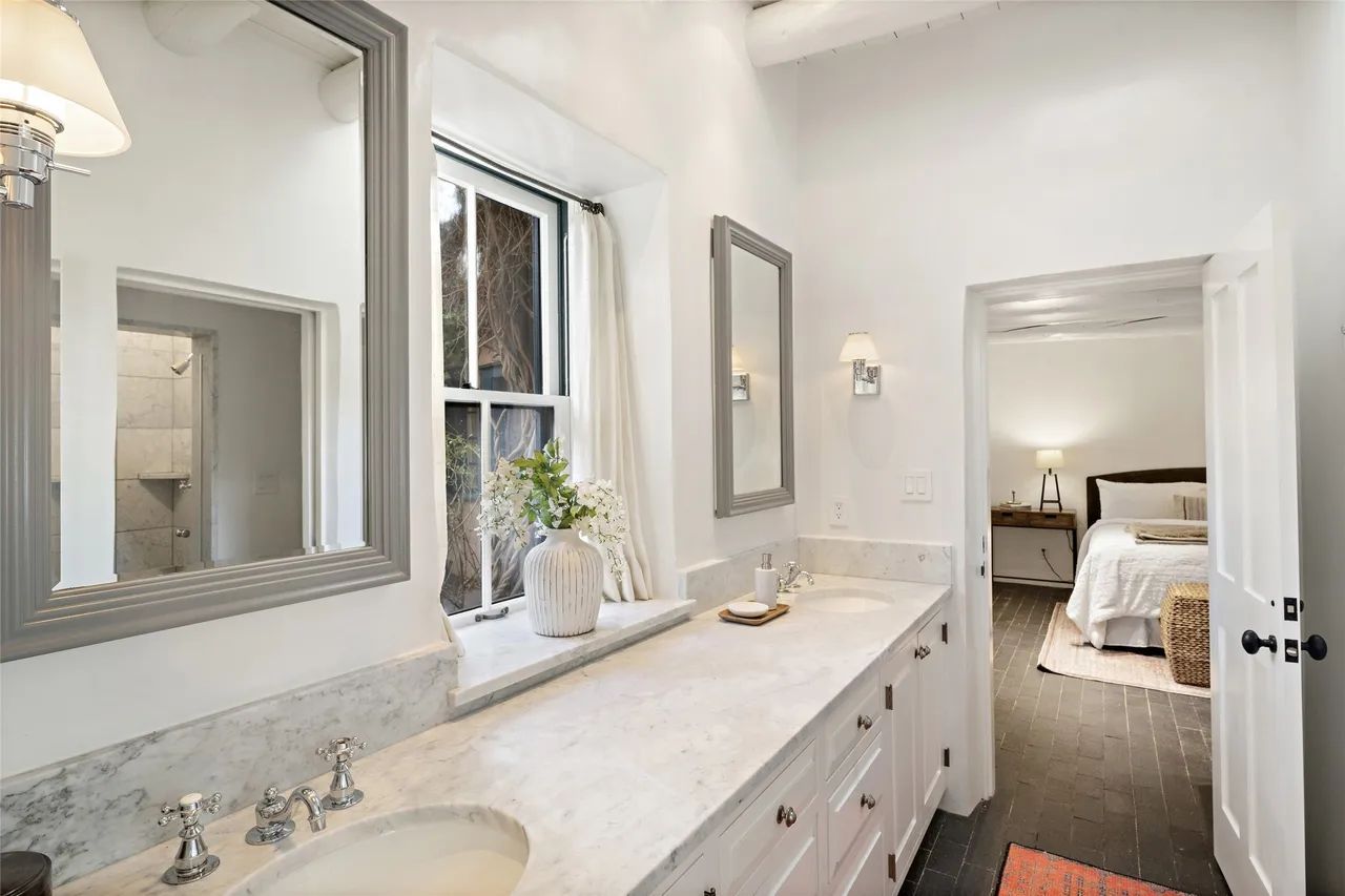 A bathroom with two sinks , two mirrors and a window.
