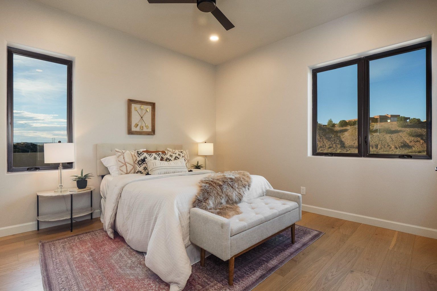 A bedroom with a bed , a bench , two windows and a ceiling fan.