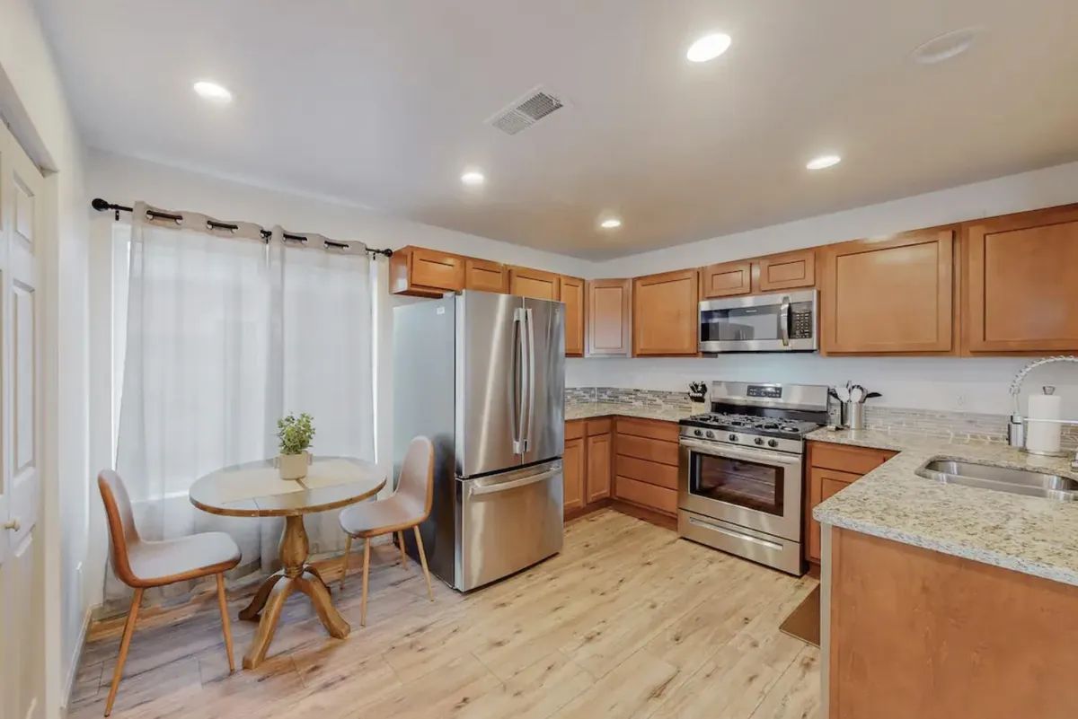 A kitchen with stainless steel appliances , wooden cabinets , a table and chairs.