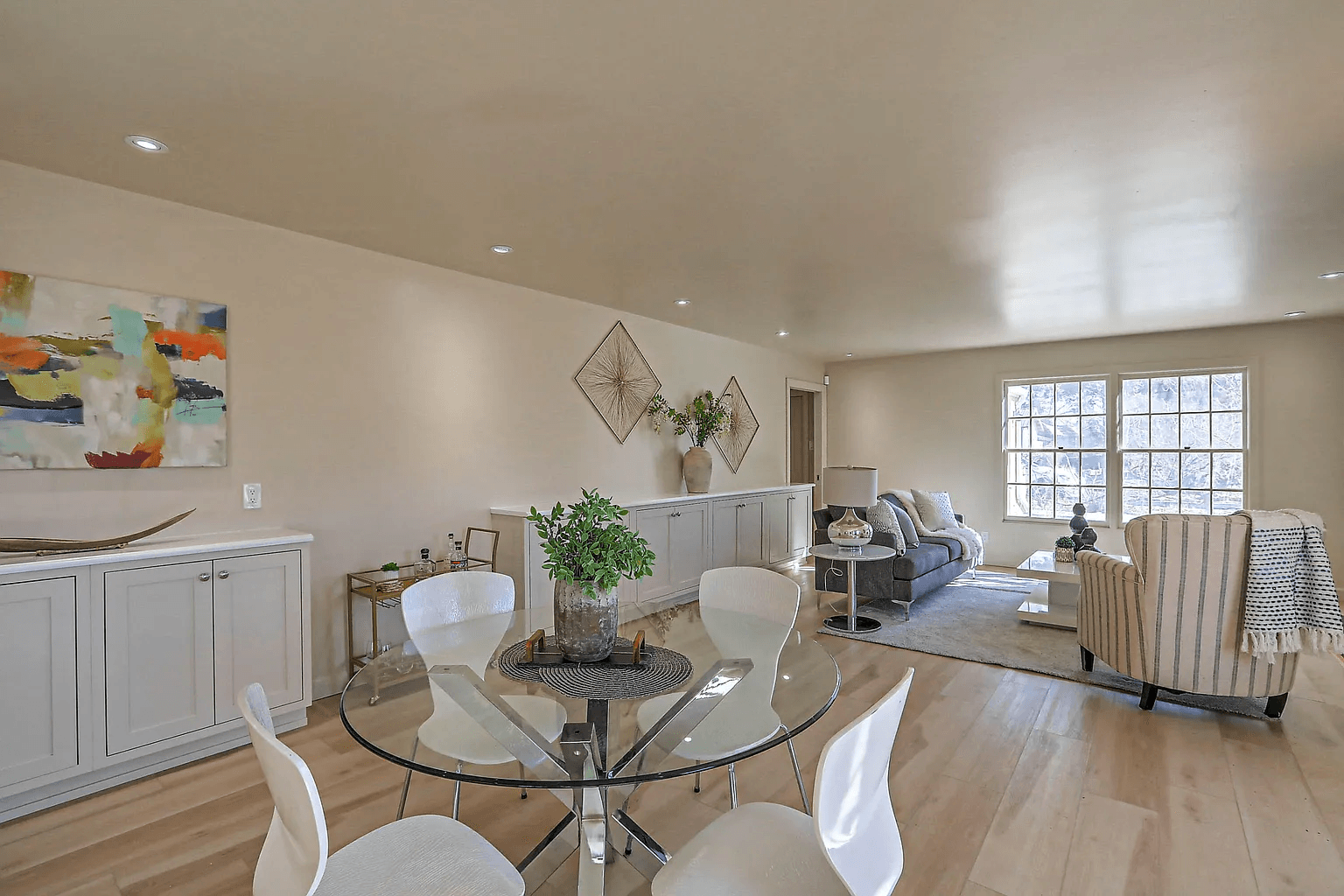 A living room with a glass table and chairs and a painting on the wall.
