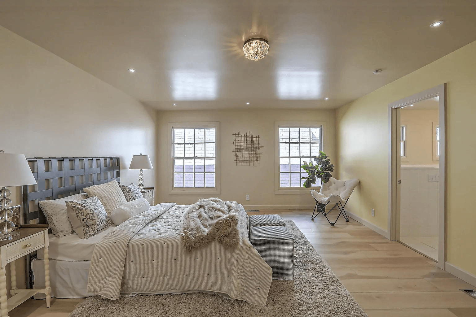 A bedroom with a bed , lamps , a rug , and two windows.