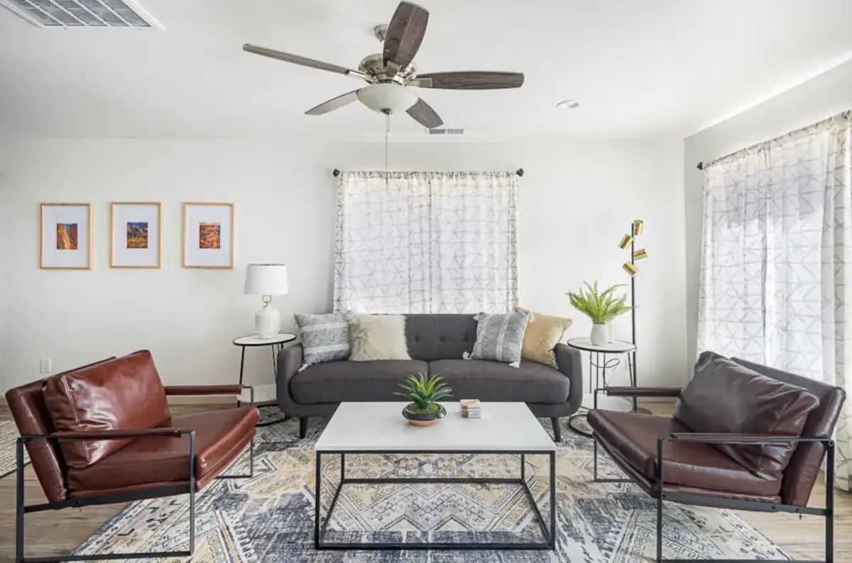 A living room with a couch , two chairs , a coffee table and a ceiling fan.
