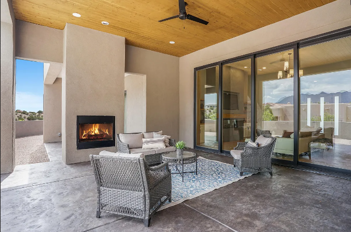 A patio with a fireplace , chairs , a table and a ceiling fan.