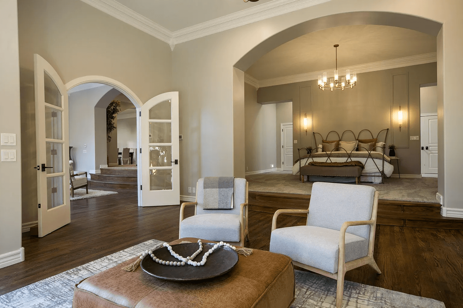 A living room with two chairs and an ottoman and a bedroom in the background.
