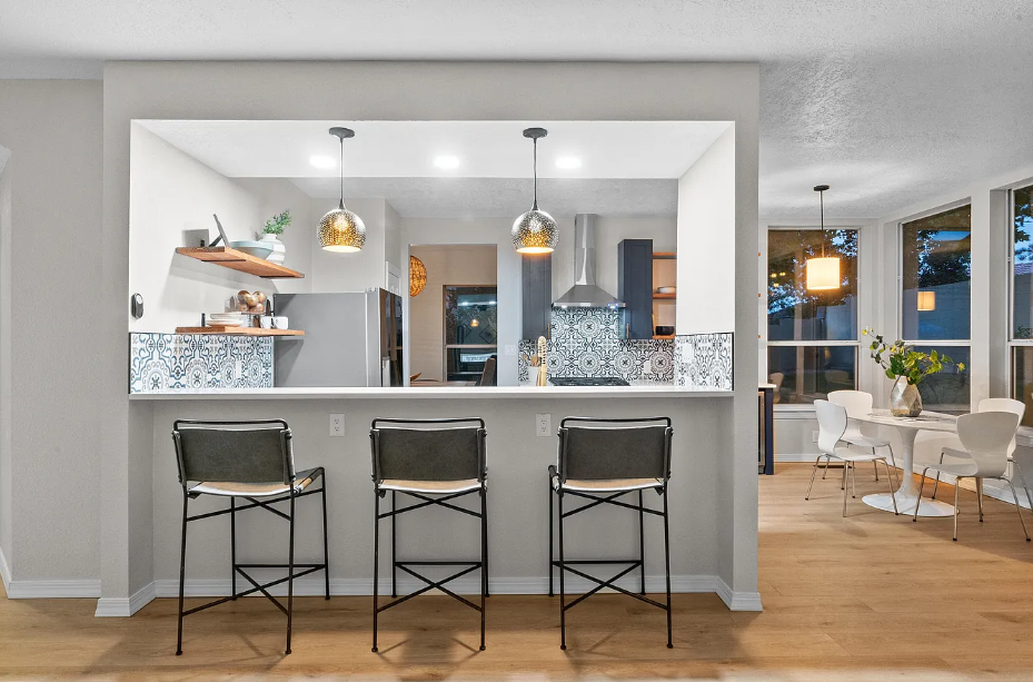 A kitchen with three bar stools and a dining room in the background.