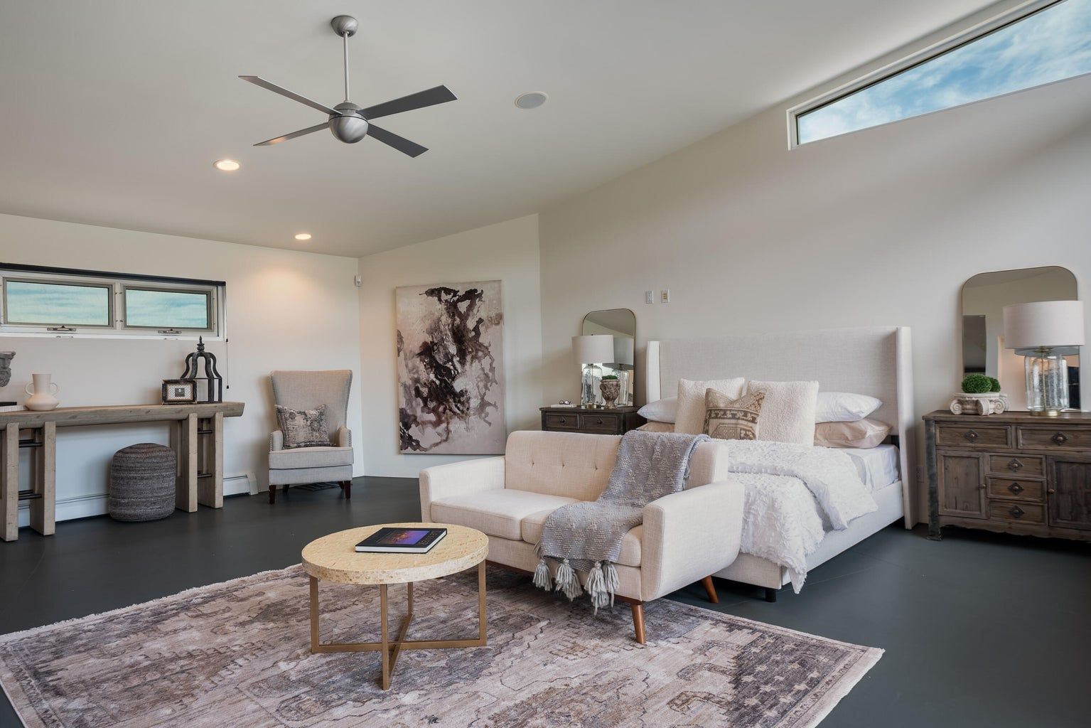 A bedroom with a large bed , couch , coffee table and ceiling fan.