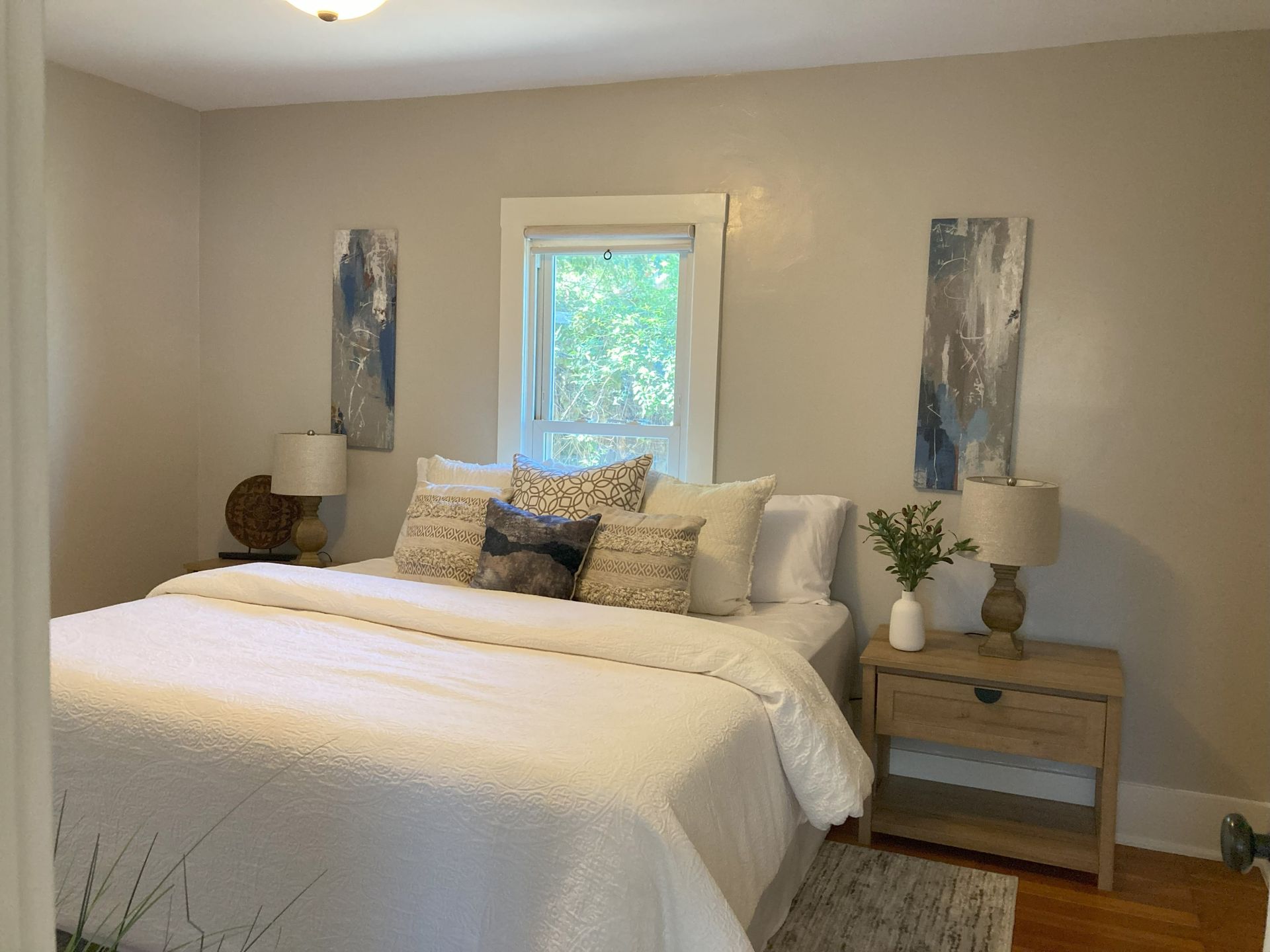 A bedroom with a bed , nightstand , lamps and two paintings on the wall.