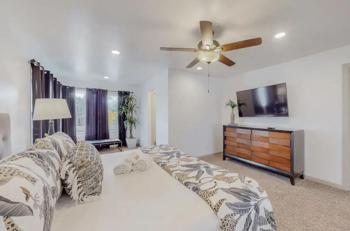 A bedroom with a bed , dresser , television and ceiling fan.