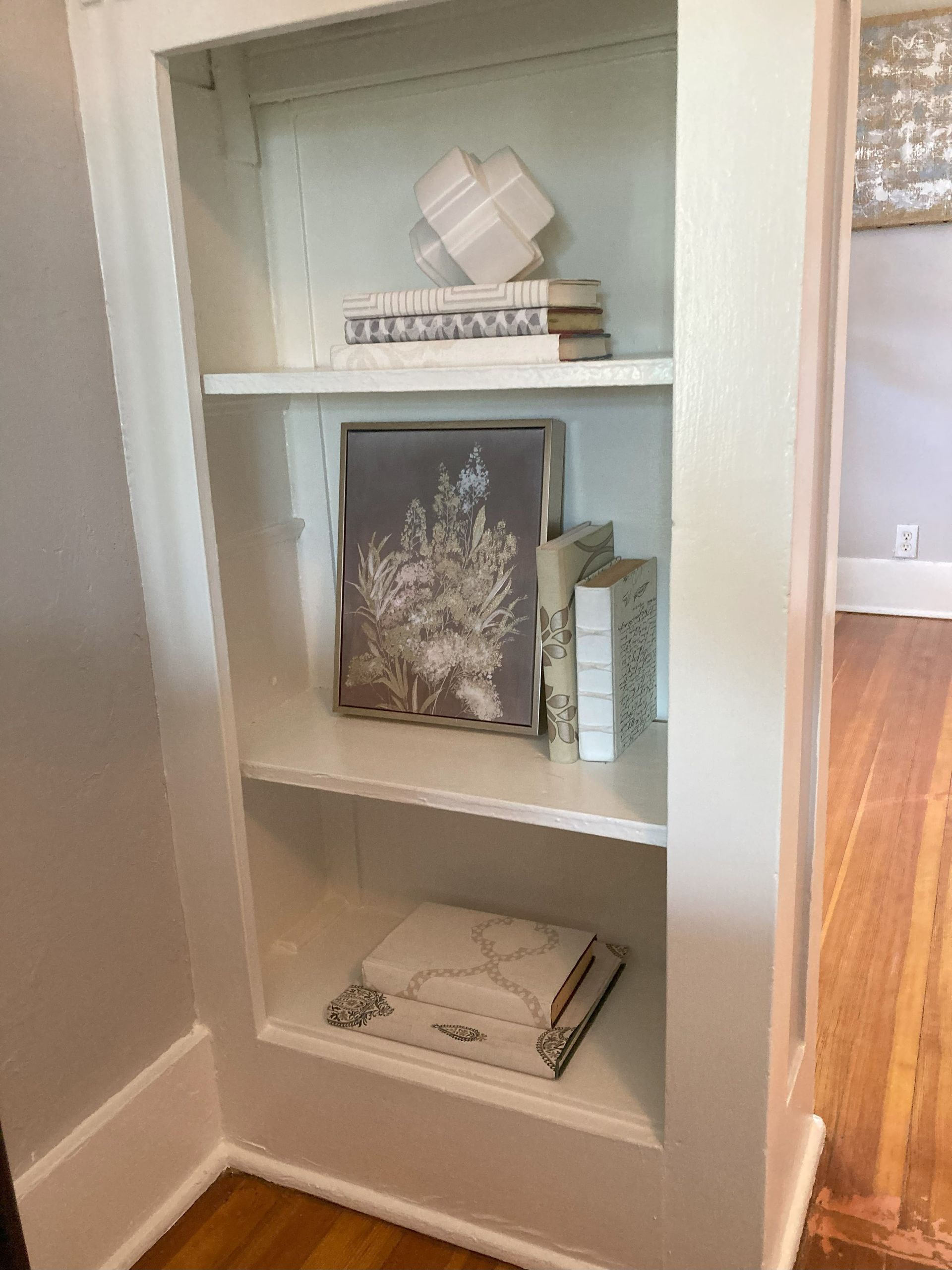 A white bookshelf with books and a painting on it.