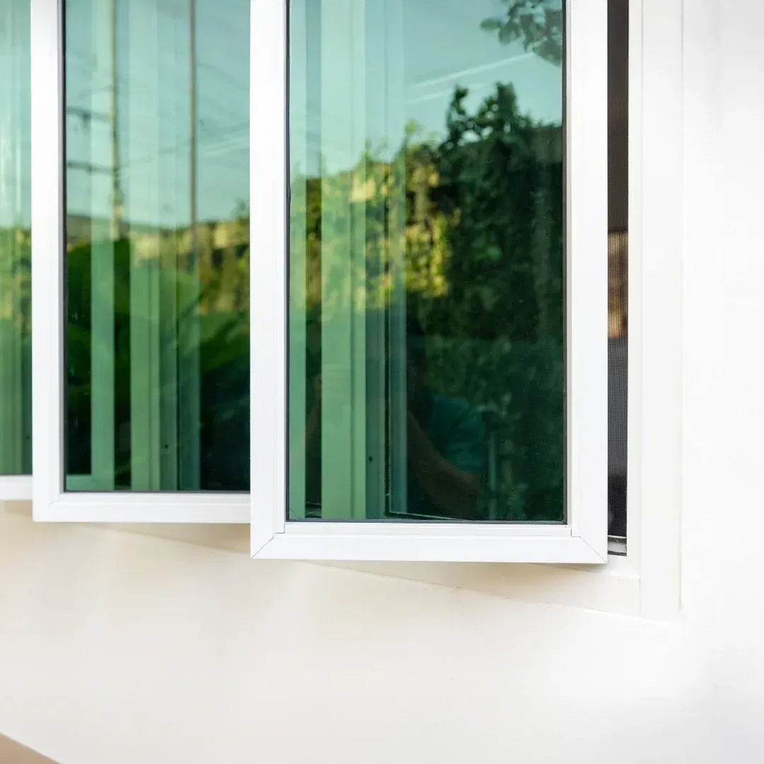 Open white-framed windows with green-tinted glass reflecting trees and sky