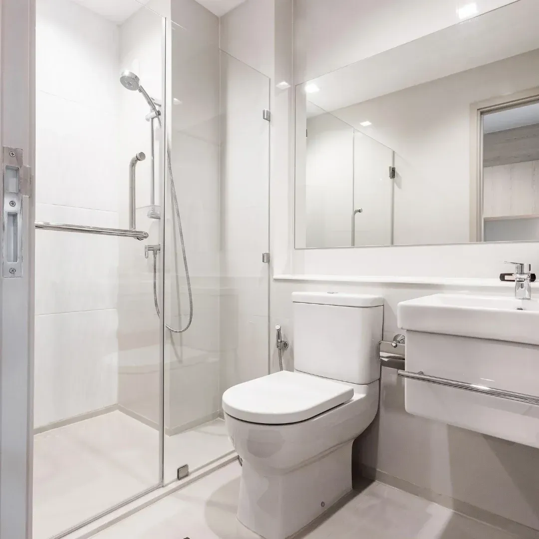 Modern white bathroom with a glass shower, toilet, sink, and large mirror