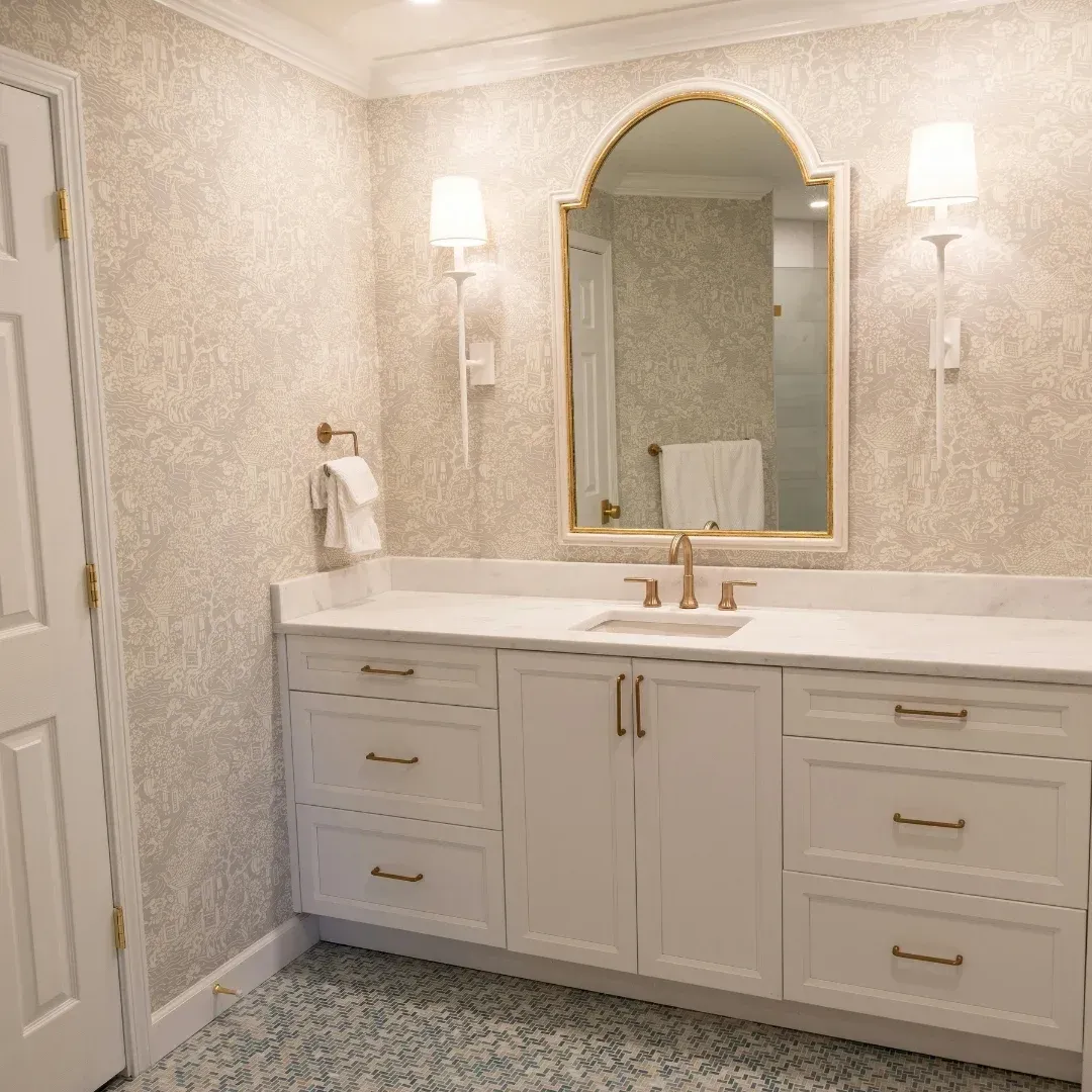 Elegant beige bathroom with white vanity, gold mirror, wall sconces, and tiled floor