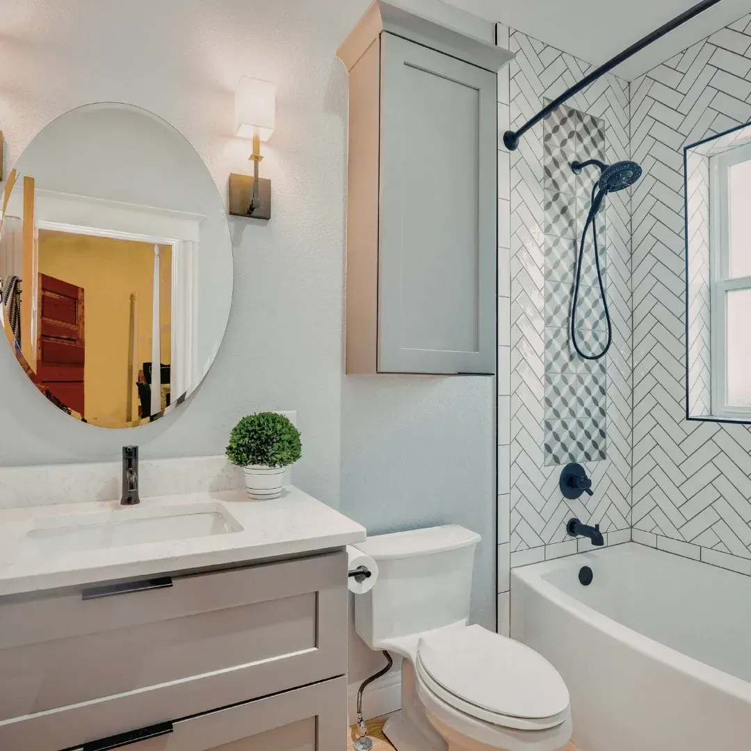 Modern bathroom with round mirror, gray vanity, white tub, and herringbone tile shower