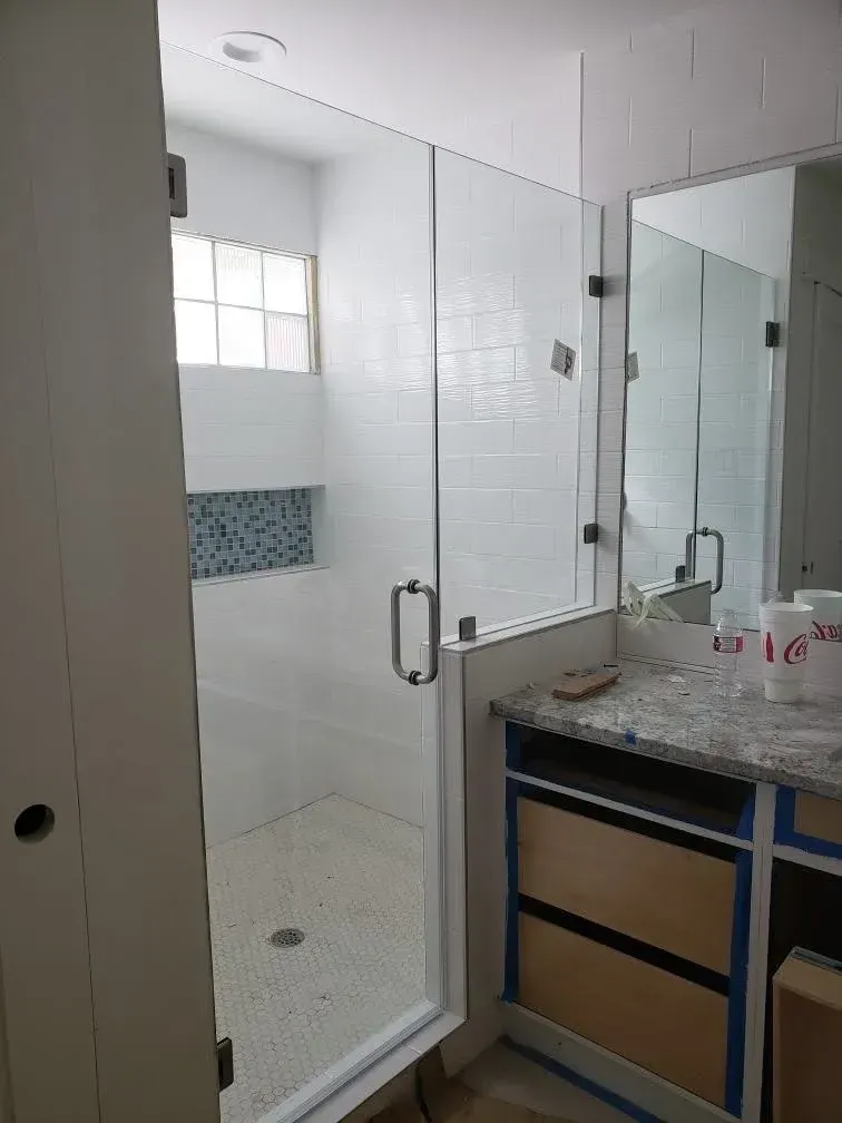 Bathroom with glass shower enclosure, white tile walls, and a vanity with a granite countertop.