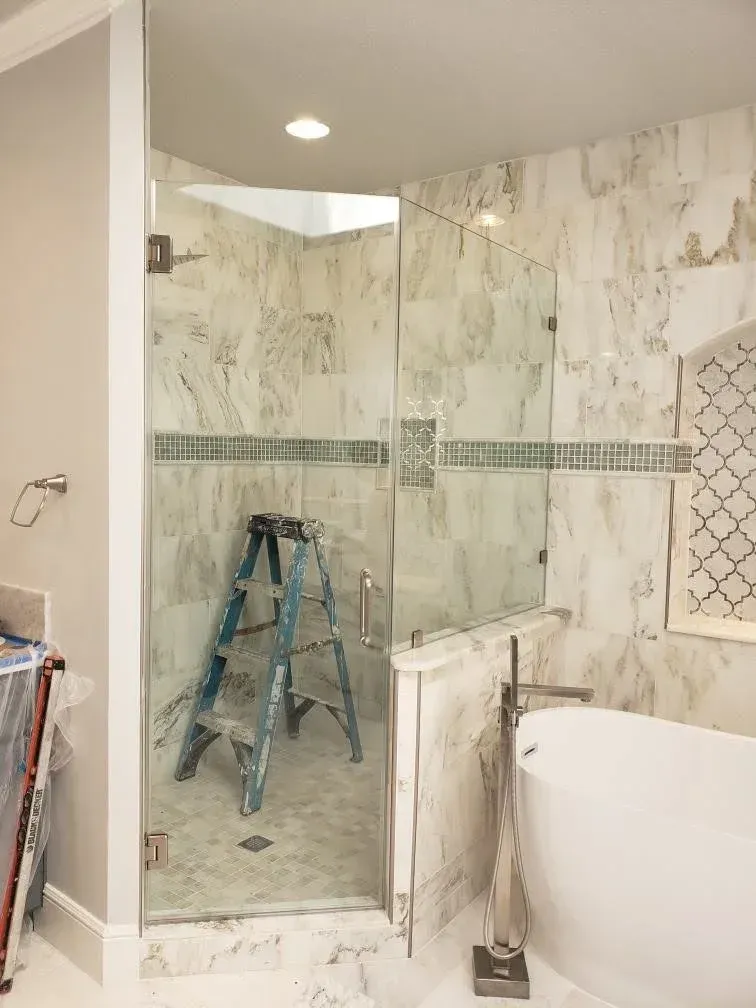 Bathroom with glass shower enclosure, marble tile, and a blue step ladder inside the shower.