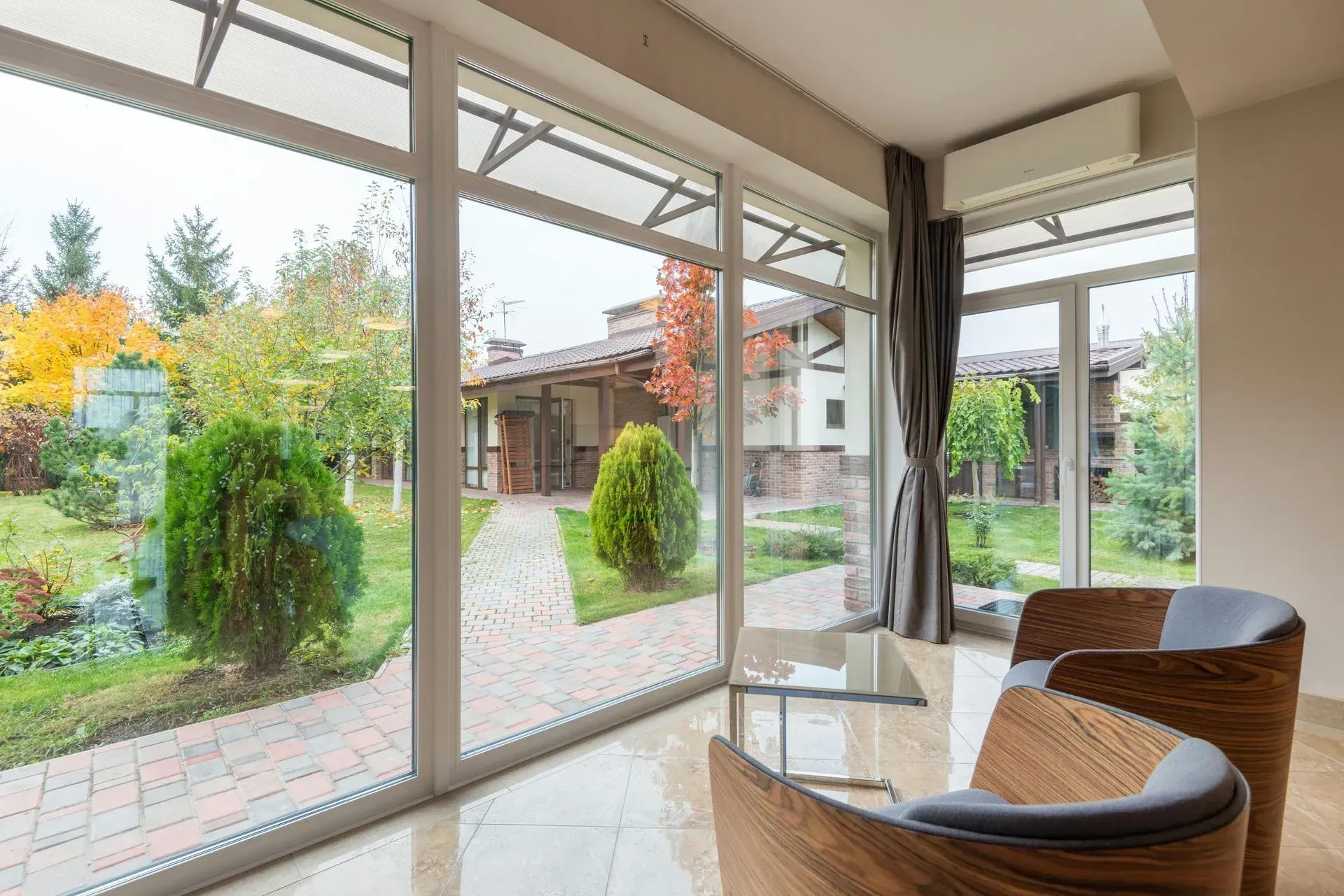 Modern sunroom with wicker chair, glass table, and large windows overlooking a garden and patio