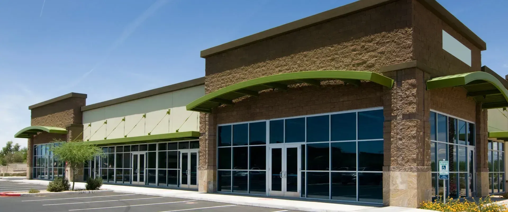 Modern commercial storefront with brick exterior, glass windows, and green awnings under a bright sky