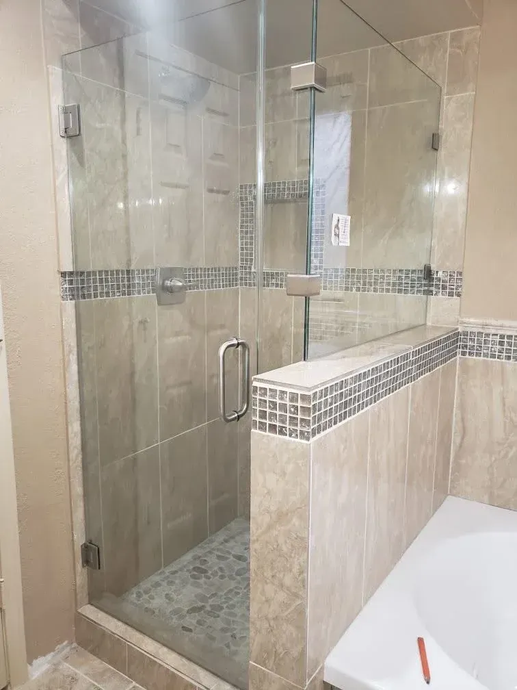 Glass-enclosed shower with beige tile, mosaic accent strip, and built-in bench in a modern bathroom