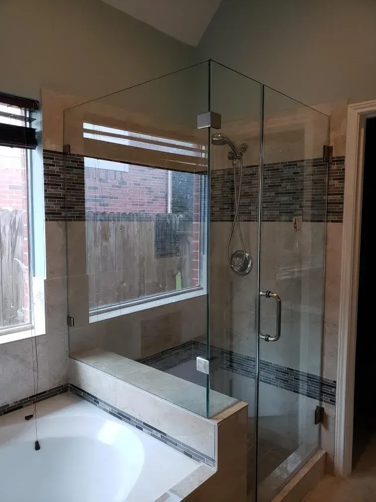 Glass-enclosed corner shower beside a bathtub in a tiled bathroom with a window.