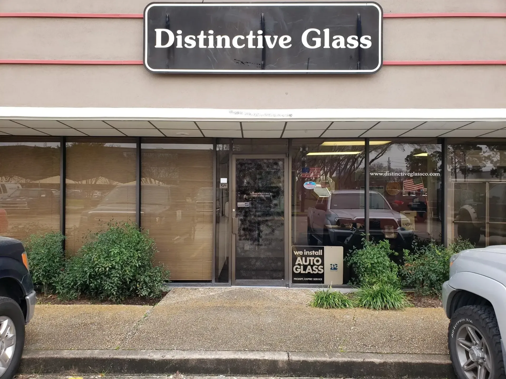 Storefront for “Distinctive Glass” with glass door, large windows, and parked vehicles on both sides.