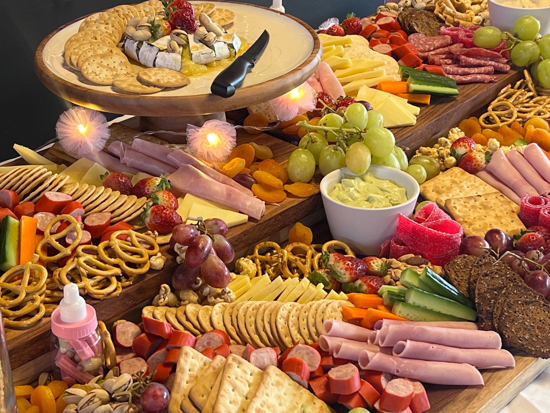 Charcuterie board with cheeses, crackers, meats, fruits, and dip, arranged on tiered wooden platters.