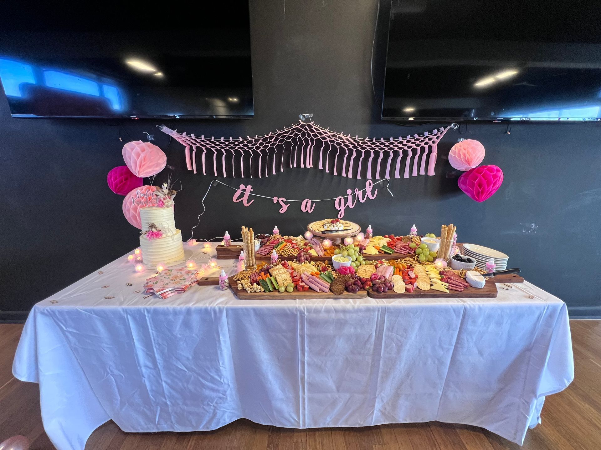 Baby shower food table with cake, charcuterie, and pink decorations. 