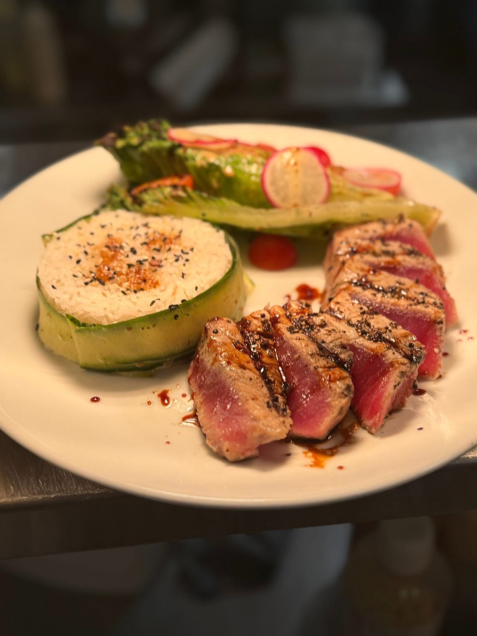 Plate of seared tuna with a rice roll and salad. Pink tuna, green rice wrap, fresh greens and radish slices.