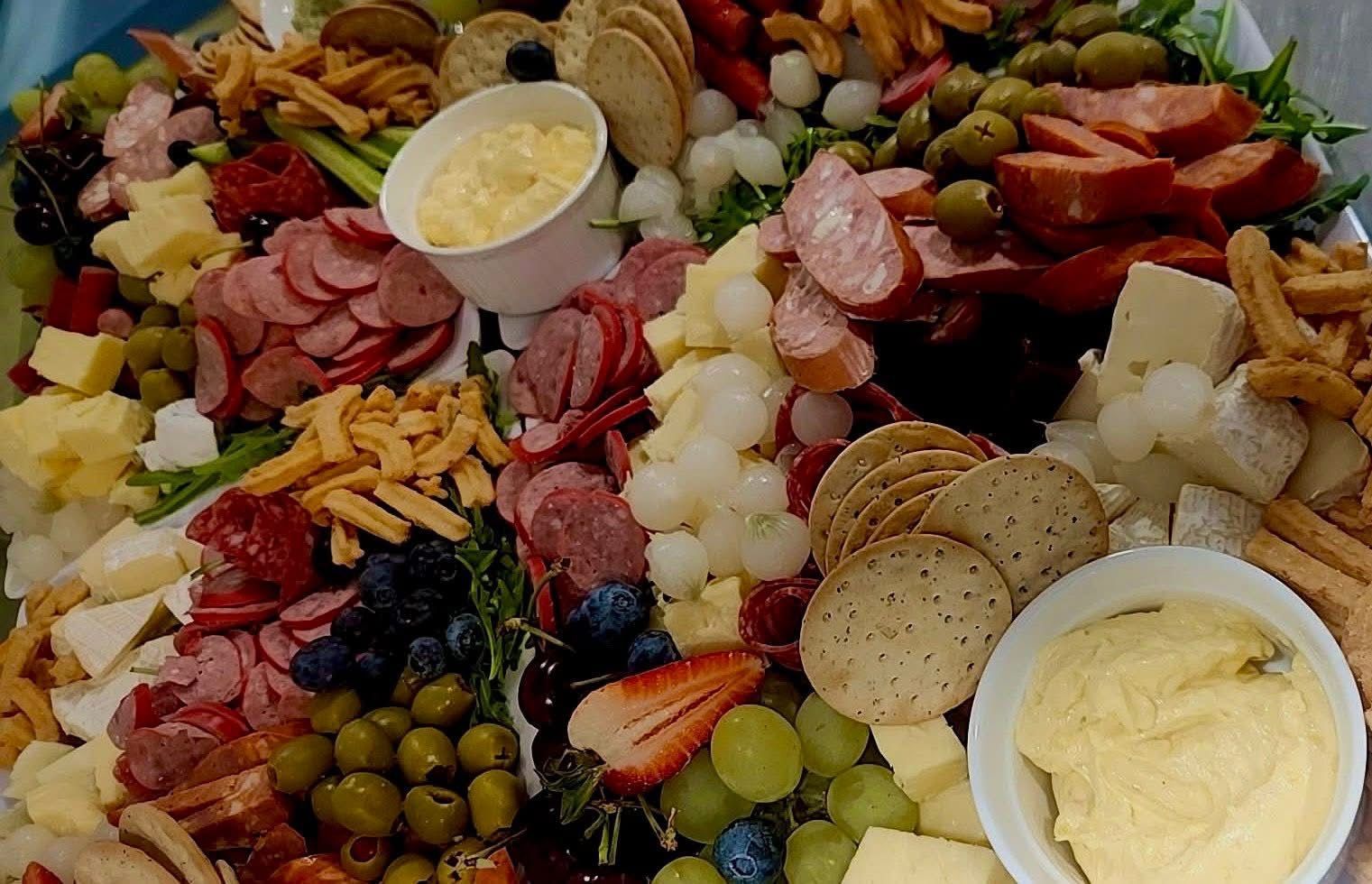 Charcuterie board with various meats, cheeses, crackers, fruits, and dips.
