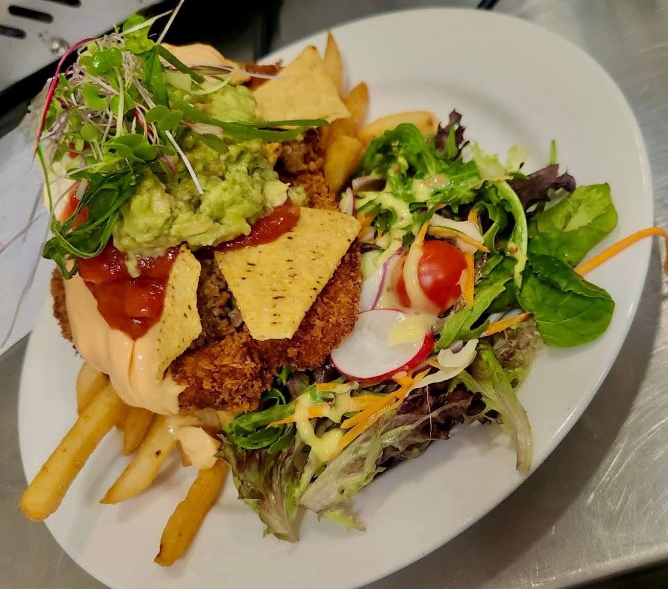 Plate of fried food: burger with guacamole, tortilla chips, fries, and salad.
