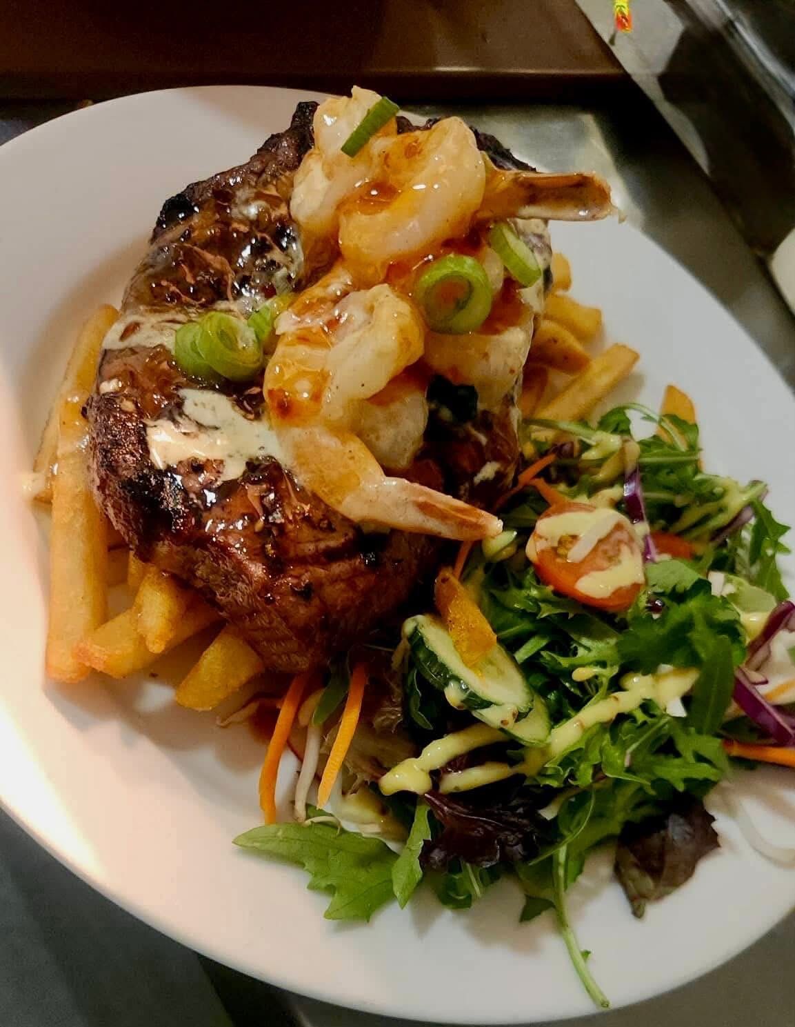 Steak topped with shrimp, fries, and salad on a white plate.