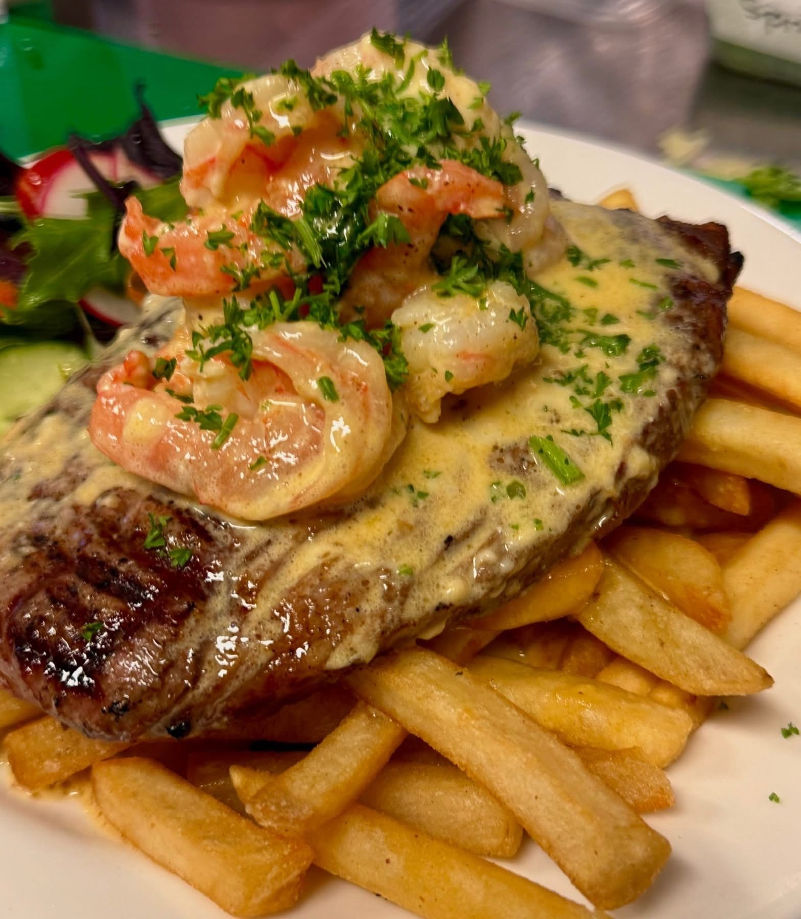 Steak with shrimp and sauce, served on fries, with salad on the side, garnished with parsley.
