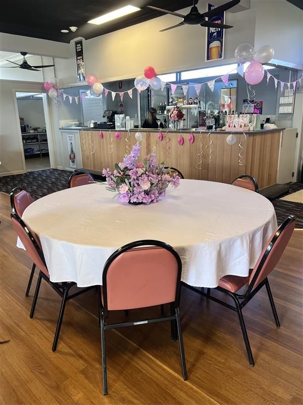 Round table set for a celebration, decorated with pink and white decor. Chairs surrounding the table.