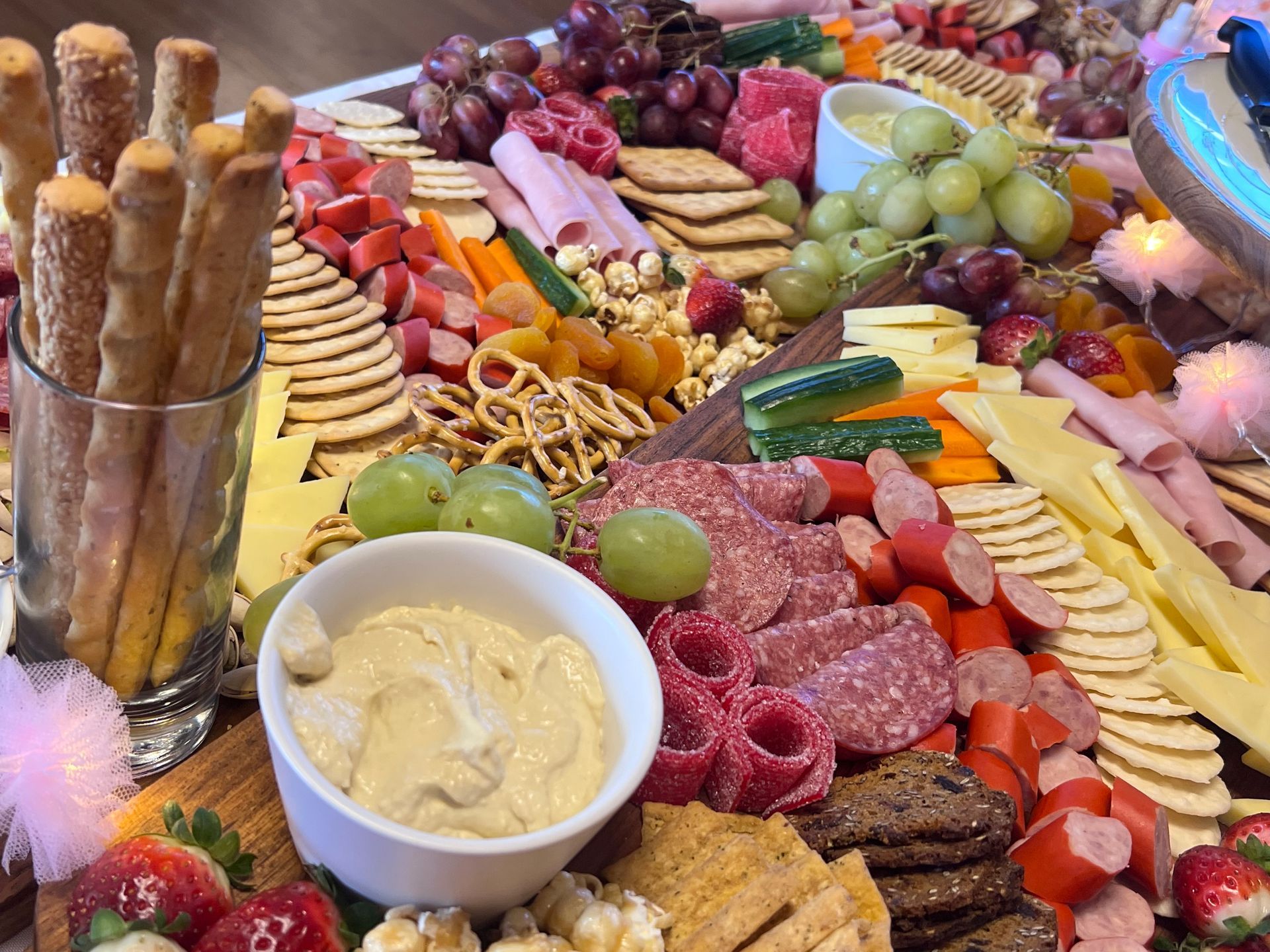Charcuterie board with various foods, including fruit, meats, cheeses, crackers, and hummus.
