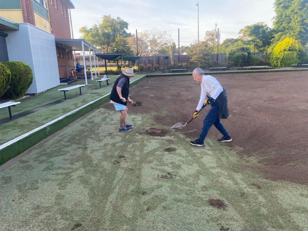 Two people repairing a lawn, one using a shovel, the other a hand tool. Outdoors.